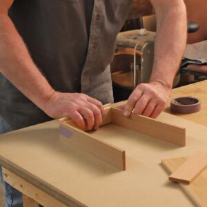 The author holds three pieces of wood that will make the front and sides of the drawer. He is taping them together.