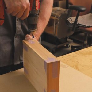 Small holes are being drilled through the sides of the drawer into front and back of the drawer.